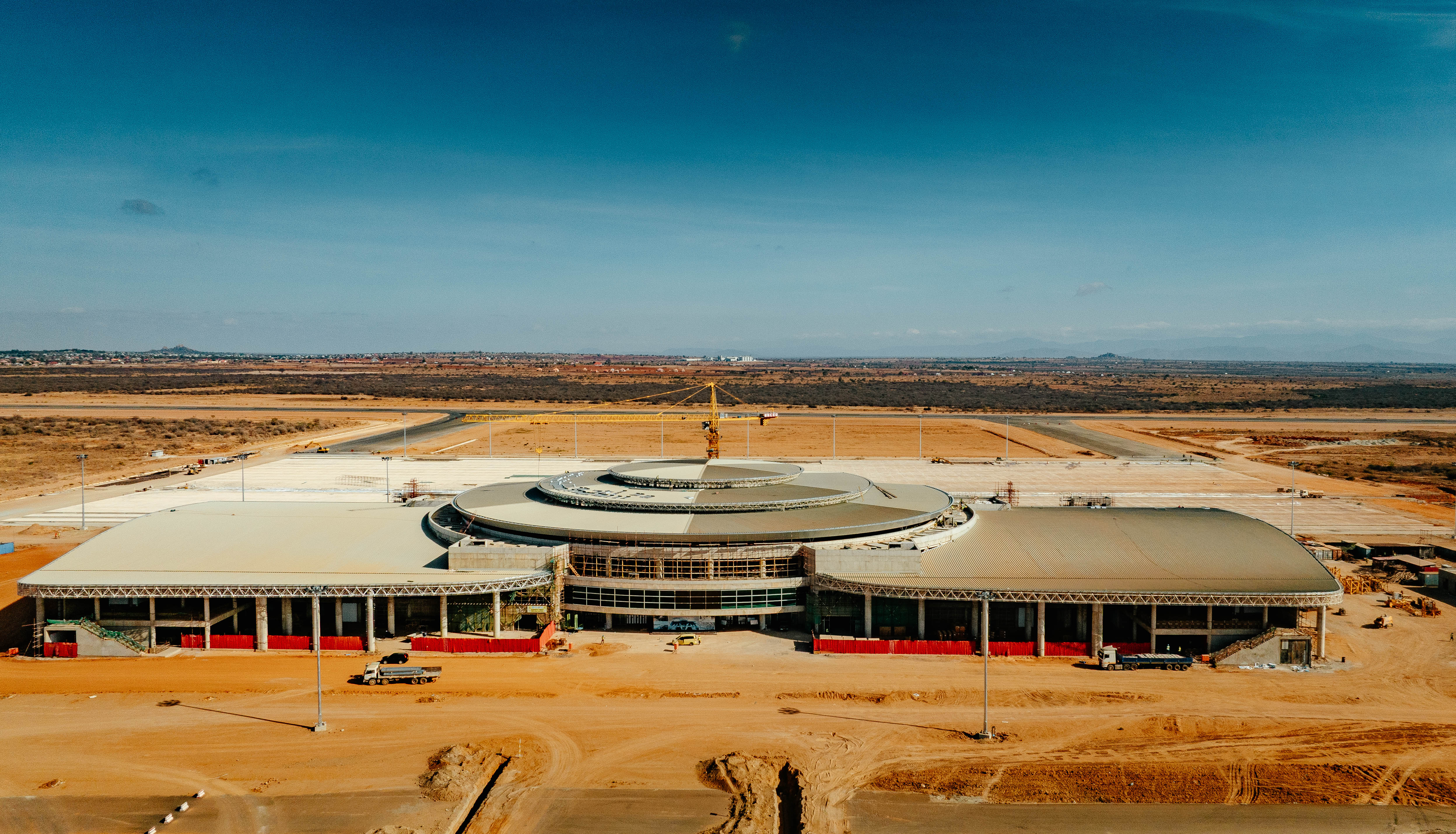 A large industrial or commercial building under construction in a vast arid landscape.