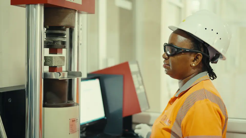 A worker in safety gear operates a machine in a laboratory setting.